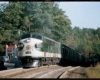 A green and white train passing by a restaurant 