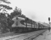 A black and white photo of a locomotive passing a stop light