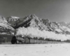 Steam powered passenger train in front of snow capped mountains