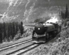 Streamlined steam locomotive on passenger train in wooded mountains