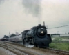 Steam locomotive departing station with train with diesel in distance