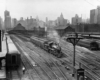 A black and white distant and overhead shot of a train leaving a station