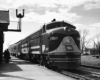 A black and white photo of a locomotive picking up passengers at a station