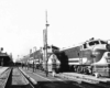 A black and white photo of two locomotives picking up passengers