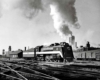 A black and white photo of a locomotive with white smoke coming out of its chimney