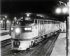 A close up black and white photo of a parked train in the dark with its lights on