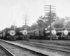 A black and white photo of five trains sitting in a rail yard