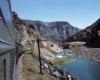 Looking back at a train as it passes through a mountain and body of water