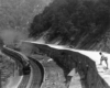 a person on a ridge watches a steam passenger train below