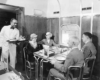 A black and white photo of four people being served food inside a train