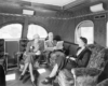 A black and white photo of three people talking inside a train