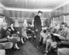 A black and white photo of a group of people sitting and talking while riding a train