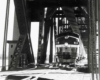 A close up black and white photo of a train coming through a bridge