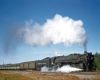 A locomotive on the track with big white smoke coming out of its chimney