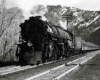 A black and white photo of a locomotive coming out of the mountains