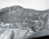 A black and white photo taken from the top of a locomotive looking back at the train and the mountains