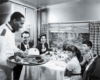 A black and white photo of a family being served food on a train