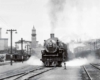 A back and white photo of a train leaving a station