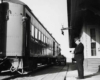 A black and white photo of the train conductor standing outside at the train station