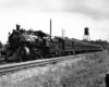 Steam locomotive with five passenger cars by semaphore signal and water tower