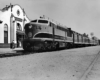 Diesel locomotive with five passenger cars in front of station