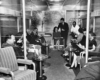 A black and white photo of people talking while sitting in a train