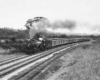 A black and white photo of a train turning a corner with smoke coming out of its chimney