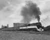 A black and white photo of a train with black smoke coming out of its chimney as it passes through a city