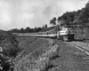 A black and white photo of a train turning a corner in a grassy area