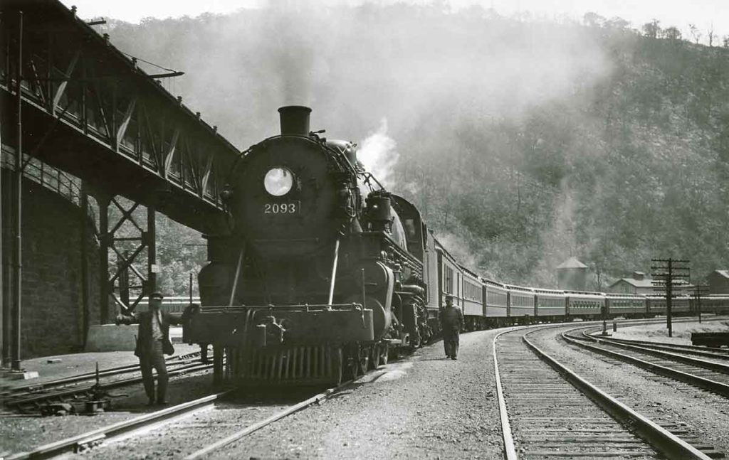 A black and white photo of a conductor posing next to a locomotive