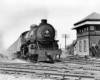 A black and white photo of a train outside a building