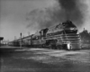 A black and white photo of a locomotive parked next to a stop light