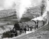 A train turning a corner with big white smoke coming out of its chimney