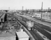 a diesel passenger train rolling by some buildings