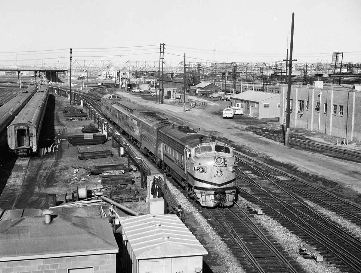 a diesel passenger train rolling by some buildings