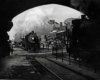 A black and white photo of a train coming toward a tunnel