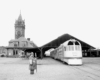 A black and white photo of a training departing the station with a person standing nearby