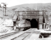 A black and white photo of a train exiting a tunnel