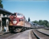 A yellow and red train passing through a town as a person crosses the tracks