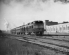 A black and white photo of a car baggage-RPO-locomotive passing buildings on the track