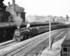 A black and white photo of a train approaching a station