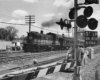 A black and white photo of a train approaching a stop light