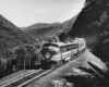 A black and white photo of a locomotive moving through the mountains