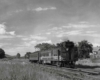 A black and white photo of a train passing through a rural town