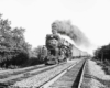 A black and white photo of a train coming down the tracks with smoke coming out of its chimney
