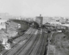 A black and white distant photo of two trains turning a corner at the same time