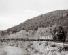 A black and white photo of a train turning a corner with black smoke coming out of its chimney