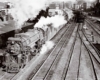 A black and white photo of two trains approaching a station