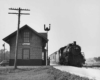 a steam engine passing a flagstop with it's mail hook extended