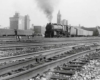 A distant shot of a train pulling into a train station with buildings in the background